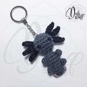 May include: A gray crocheted axolotl keychain with black crocheted gills. The keychain has a silver metal ring.