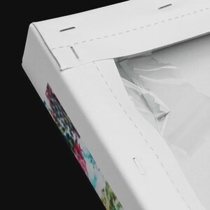 May include: A white canvas print stretched over a wooden frame, viewed from the back corner. The white canvas material is pulled taut and secured with metal staples along the wooden frame edges. A small metal sawtooth hanger is attached.
