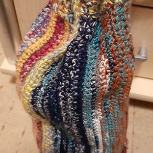 Könnte beinhalten: Handgefertigte Häkeltasche in verschiedenen Farben, darunter Gelb, Blau, Orange und Weiß. Die Tasche hat einen Kordelzugverschluss und eine rosa Schlaufe zum Aufhängen. Die Textur des Garns ist sichtbar.