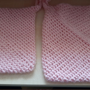 Könnte beinhalten: Zwei rosa gestrickte Quadrate, möglicherweise Topflappen oder Geschirrtücher, mit einem Verbindungsstück.