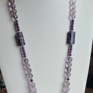 May include: A long amethyst necklace with a large, faceted amethyst pendant. The necklace is made of round and rectangular amethyst beads.