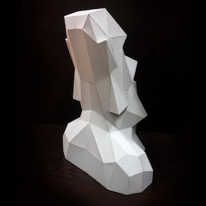 May include: A white paper sculpture of a geometric shape, resembling a stylized human figure. The sculpture is made of folded paper and has a textured surface.