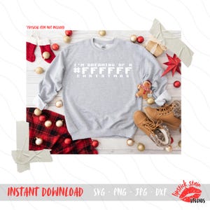 May include: A gray sweatshirt with the text "I'm dreaming of a #FFFFFF Christmas" printed in white on the front. The sweatshirt is surrounded by Christmas decorations, including red and gold ornaments, a gingerbread man, and a red and white plaid blanket.