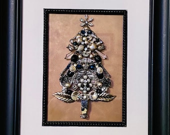 May include: A framed artwork featuring a Christmas tree made of rhinestones and other decorative elements. The tree is black, silver, and white, and is set against a gold background.
