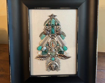 May include: A framed artwork featuring a turquoise and silver Christmas tree made of various beads, charms, and feathers. The tree is decorated with a small image of the Virgin Mary.