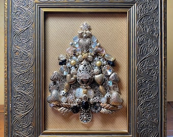 May include: A framed Christmas tree made of various jewelry and trinkets, including hearts, beads, and rhinestones. The tree is decorated with a star on top and is set against a beige background.
