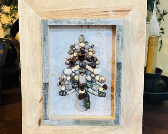 May include: A framed artwork featuring a Christmas tree made of various beads and stones in shades of brown, white, and gray. The tree is set against a white background with a gray frame.
