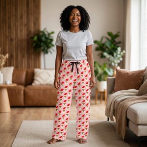 Op de afbeelding: Een lichtgrijs T-shirt met korte mouwen gecombineerd met een lichtroze pyjamabroek met een herhalend patroon van kerstmangezichten met rode mutsen. De broek heeft een zwart trekkoord bij de elastische tailleband en rechte pijpen.