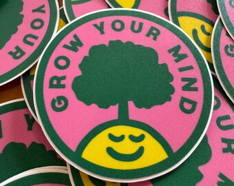 May include: A circular sticker featuring a pink background with a dark green tree growing out of a yellow smiling face. The text GROW YOUR MIND is printed in dark green capital letters around the top edge of the sticker, encircling the central design.