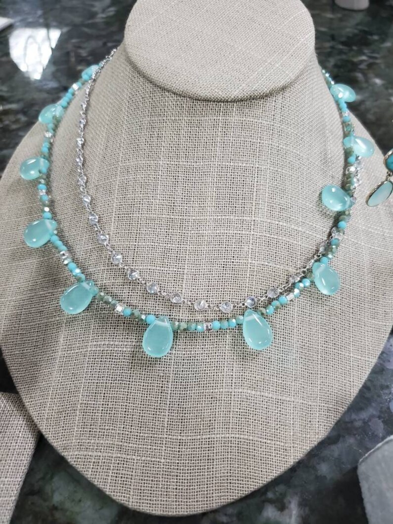 Puede incluir: Un collar de varias capas con una cadena de plata y cuentas turquesas. El collar presenta piedras turquesas en forma de l&aacute;grima que cuelgan de la cadena.