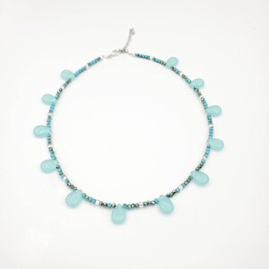 Puede incluir: Un collar delicado con una cadena plateada y cuentas de color azul turquesa. El collar presenta una serie de colgantes en forma de l&aacute;grima de piedra preciosa azul claro.