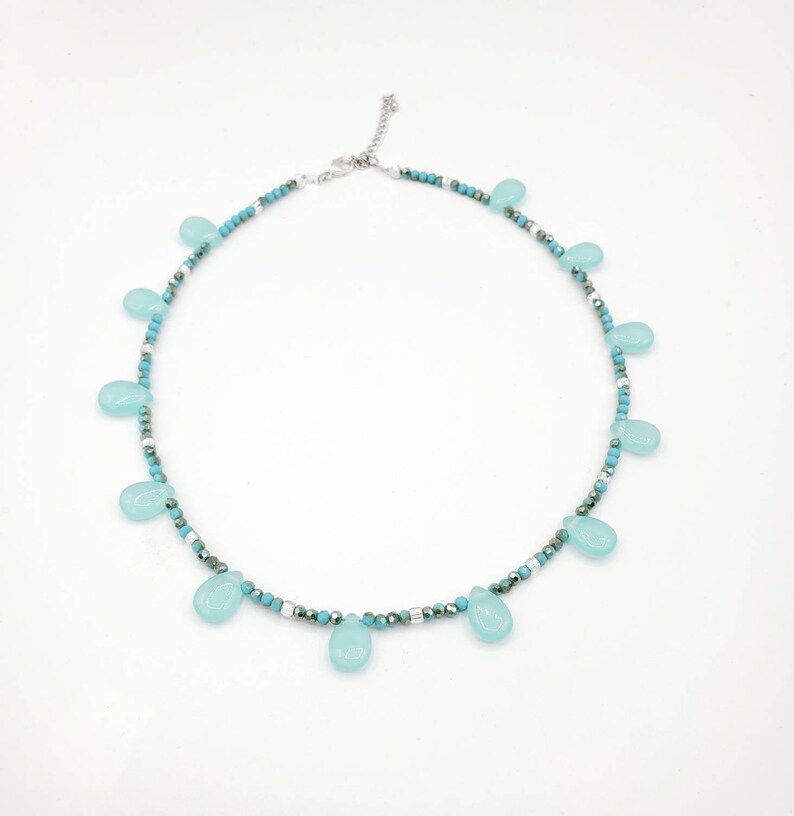 Puede incluir: Un collar delicado con una cadena plateada y cuentas de color azul turquesa. El collar presenta una serie de colgantes en forma de l&aacute;grima de piedra preciosa azul claro.