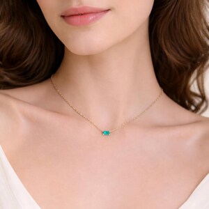 May include: A delicate gold necklace featuring a small, rectangular turquoise stone pendant. The necklace is a simple, elegant design, perfect for everyday wear. The chain is fine and the pendant is a vibrant teal color. The necklace is shown on a person's neck.