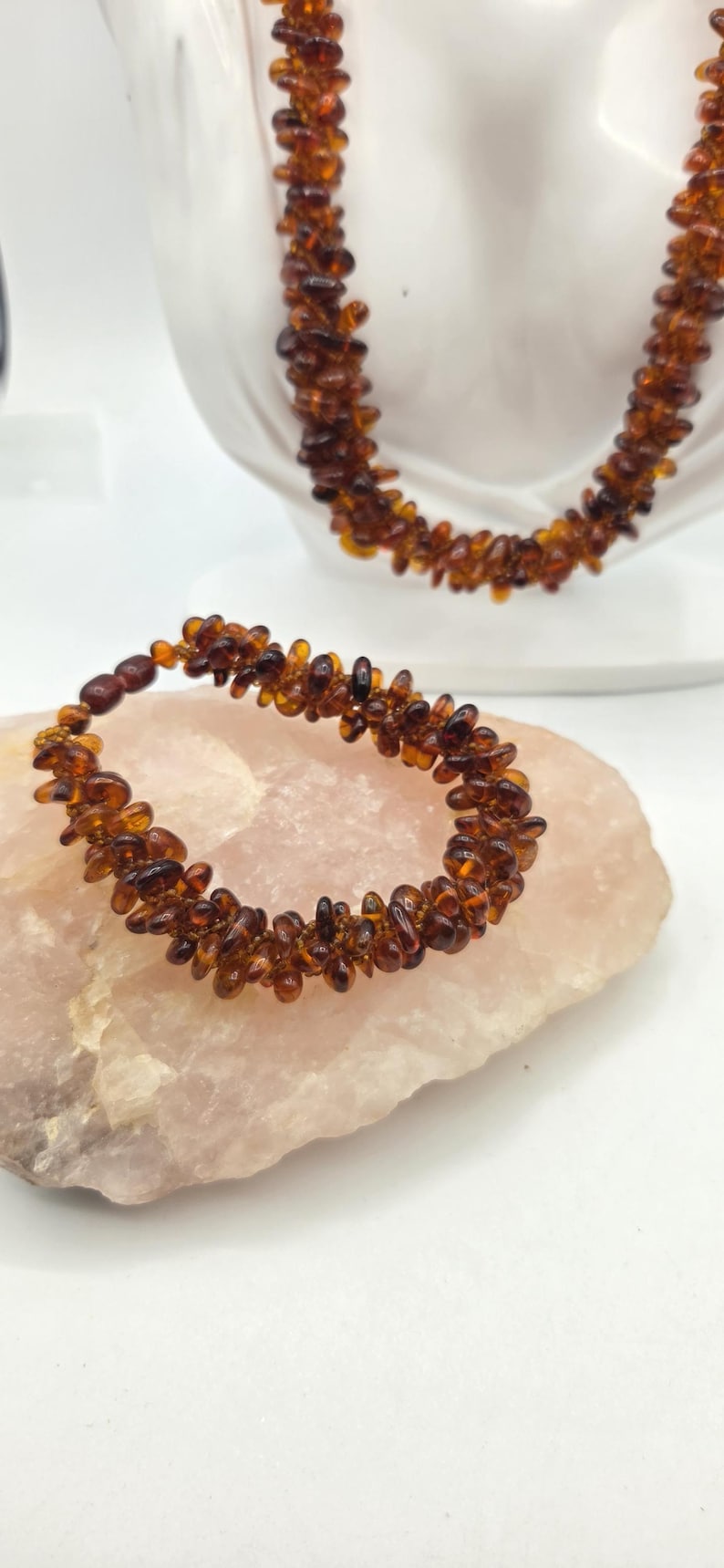 May include: A bracelet and a necklace made of small, polished, translucent amber beads in shades of deep cognac and honey brown. The beads are irregularly shaped and strung together to create a textured, multi-layered appearance.