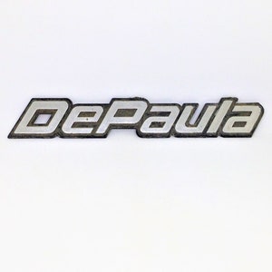 Puede incluir: Un logotipo de la Universidad DePaul de metal plateado con un contorno negro.