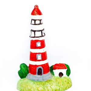 Könnte beinhalten: Ein roter und weißer Miniatur-Leuchtturm mit einem kleinen Haus daneben, beides auf einem grünen Grasgrund.