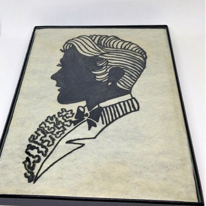 May include: Black and white silhouette of a person with a bow tie and a patterned shirt, framed in a black frame.