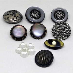 May include: Assortment of vintage buttons in various colors and materials, including silver, black, white, and iridescent. Some buttons have a textured surface, while others have a smooth finish.