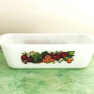 Puede incluir: Un molde rectangular de vidrio lechoso blanco con un estampado gráfico colorido de varias verduras frescas, incluyendo tomates rojos, zanahorias naranjas, lechuga verde y cebollas moradas centrado en el lado frontal exterior.