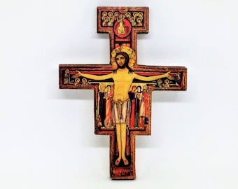 May include: A wooden cross featuring a central painted figure of a person with long dark hair and a halo, arms outstretched. The cross is decorated with smaller painted figures in red, blue, and gold tones along the horizontal and vertical beams.