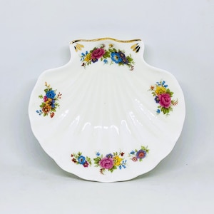 May include: A white, shell-shaped dish with a scalloped edge and a gold trim. The dish is decorated with clusters of colorful flowers in shades of pink, blue, yellow, and orange. The dish is likely made of porcelain.