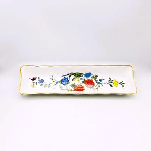 Könnte beinhalten: Eine rechteckige weiße Keramikschale mit goldenem Rand und floralem Design. Die Blumen sind in Blau-, Rot-, Gelb- und Lilatönen gehalten. Die Schale ist leer und steht auf weißem Hintergrund.