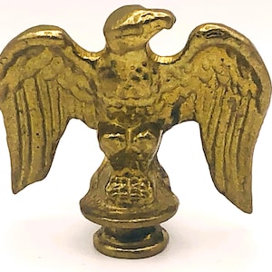 Puede incluir: Una detallada figura de águila dorada con las alas extendidas. El águila tiene una superficie texturizada y está montada sobre una base decorativa. La figura es probablemente de metal y es un objeto decorativo.