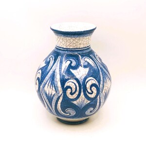 May include: A ceramic vase with a round body and a narrow neck. The vase is primarily blue with a white, crackled pattern around the neck and a swirling design on the body. The base is a darker shade of blue.