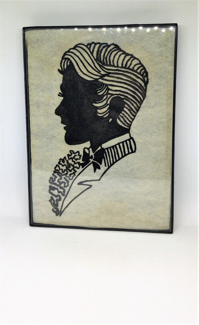 May include: A black and white silhouette of a person with a bow tie and a patterned collar, framed in a black frame.