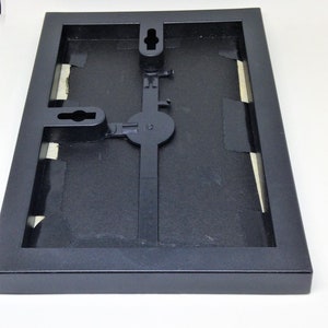 May include: Black picture frame with a hanging mechanism on the back. The frame is made of wood and has a matte finish.