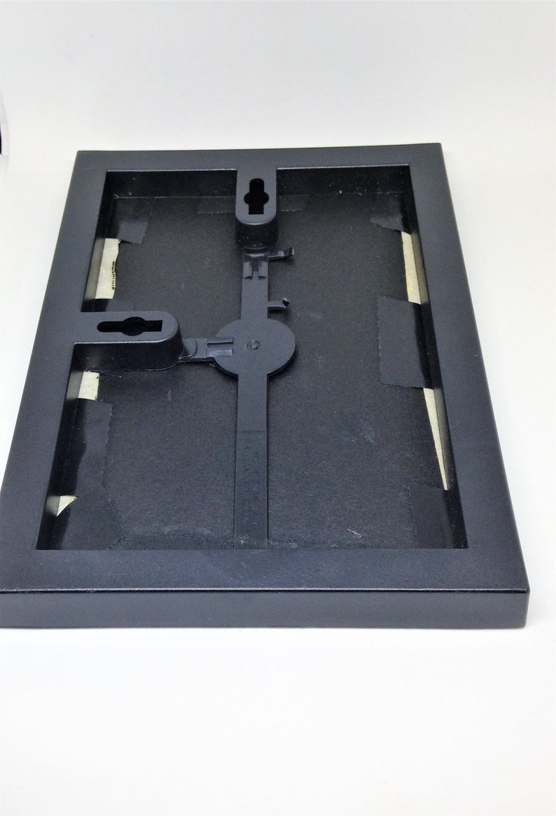 May include: Black picture frame with a hanging mechanism on the back. The frame is made of wood and has a matte finish.