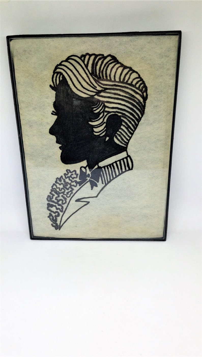 May include: A black and white silhouette of a person with a bow tie and a patterned shirt, framed in a black frame.