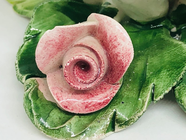 May include: A ceramic rose with pink petals and green leaves. The rose is the focal point, with detailed veining on the leaves. The piece appears to be a decorative item, possibly for a home decor.
