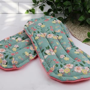 May include: Two reusable cloth menstrual pads. The pads have a teal background with a floral pattern in yellow, pink, and white. The edges are trimmed with a pink fabric.
