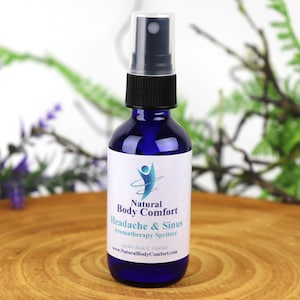 May include: A blue glass bottle with a black spray nozzle and a white label that reads "Natural Body Comfort Headache & Sinus Aromatherapy Spritzer" and "www.NaturalBodyComfort.com".