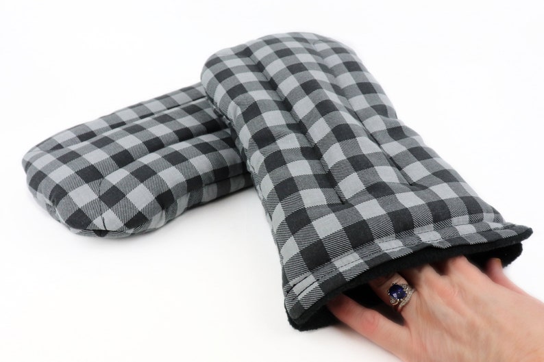 K&ouml;nnte beinhalten: Ein Paar Ofenhandschuhe in Schwarz-Wei&szlig;-Karos mit schwarzem Fleece-Futter. Die Handschuhe sind gesteppt und haben eine dicke Isolierschicht zum Schutz vor Hitze.