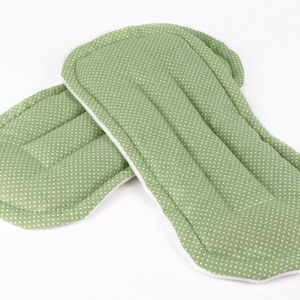 May include: Two green cloth menstrual pads with white polka dots. The pads have a rectangular shape with rounded edges and are made of soft, absorbent material. The pads are designed for feminine hygiene.