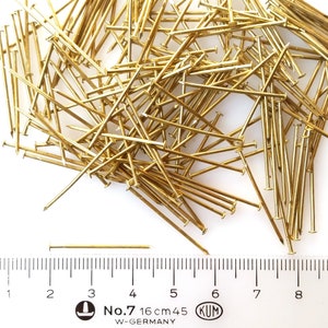 Puede incluir: Un mont&oacute;n de tachuelas o chinchetas doradas con una regla para la escala. La regla muestra medidas en cent&iacute;metros y pulgadas. El texto en la regla dice "No. 7 16 cm 45 KUM W-GERMANY".