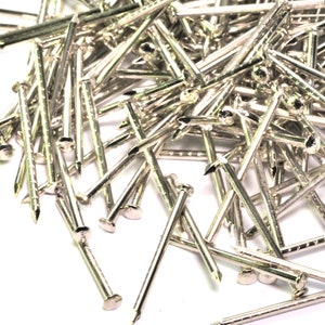 May include: A large pile of silver-colored tacks or finishing nails. The tacks are arranged in a random pattern and are all the same size.