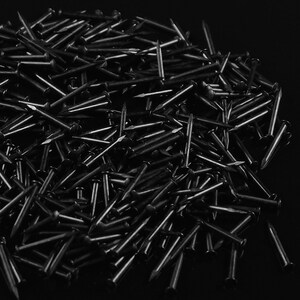 K&ouml;nnte beinhalten: Ein gro&szlig;er Haufen schwarzer Metalln&auml;gel. Die N&auml;gel sind alle gleich gro&szlig; und gleich geformt und in einem zuf&auml;lligen Muster angeordnet.