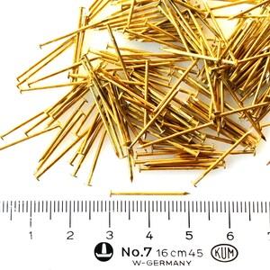 Puede incluir: Un mont&oacute;n grande de tachuelas o clavos de color dorado, con una regla que muestra una medida de 16 cm. La regla tambi&eacute;n tiene el texto "No. 7 16 cm 45 KUM W-GERMANY".