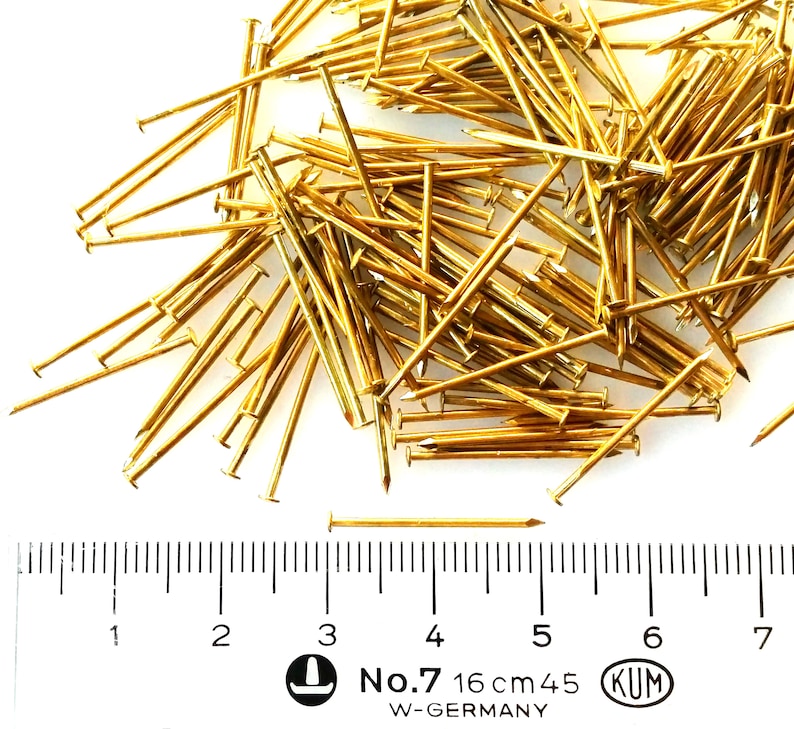 Puede incluir: Un mont&oacute;n grande de tachuelas o clavos de color dorado, con una regla que muestra una medida de 16 cm. La regla tambi&eacute;n tiene el texto "No. 7 16 cm 45 KUM W-GERMANY".