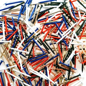 Pode incluir: Um grande sortimento de tachinhas coloridas em vermelho, branco, azul, preto, dourado e cobre. As tachinhas est&atilde;o espalhadas sobre uma superf&iacute;cie branca.