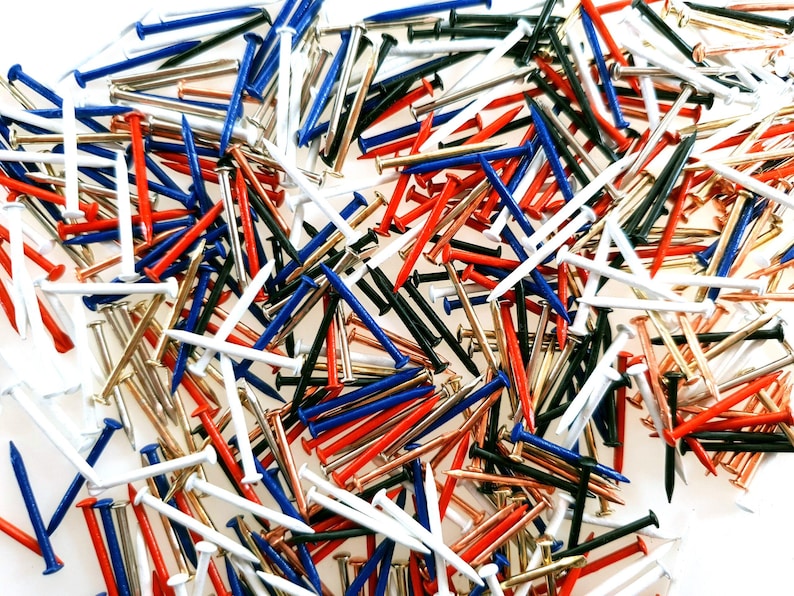 Pode incluir: Um grande sortimento de tachinhas coloridas em vermelho, branco, azul, preto, dourado e cobre. As tachinhas est&atilde;o espalhadas sobre uma superf&iacute;cie branca.