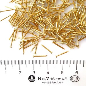 Puede incluir: Un mont&oacute;n de tachuelas o clavos de color dorado, que miden 16 cm de largo, con una regla para la escala. Las tachuelas est&aacute;n etiquetadas como "No. 7" y "KUM W-GERMANY".
