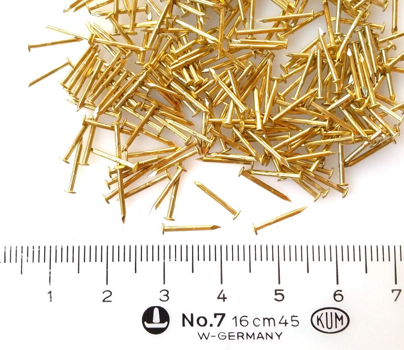Puede incluir: Un mont&oacute;n de tachuelas o clavos de color dorado, que miden 16 cm de largo, con una regla para la escala. Las tachuelas est&aacute;n etiquetadas como "No. 7" y "KUM W-GERMANY".