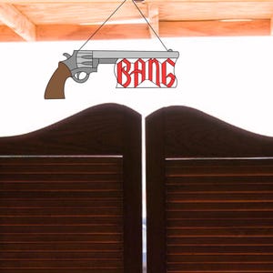 Op de afbeelding: Een paar bruine houten saloon deuren met een bord erboven. Het bord is een witte rechthoek met een cartoontekening van een revolver en het woord "BANG" in rode letters.
