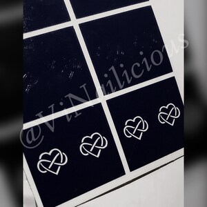 Peut inclure: Une feuille de pochoirs à ongles noirs avec quatre motifs de cœurs infinis blancs. Les pochoirs sont disposés en grille. Le texte "@ViNailcious" est visible dans le coin inférieur gauche de l'image.