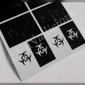 Könnte beinhalten: Eine Blatt mit schwarzen Vinyl-Aufklebern mit einem Biohazard-Symbol-Design. Die Aufkleber sind in einem Raster angeordnet.