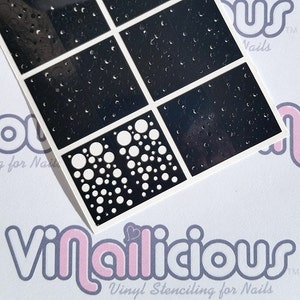 May include: A sheet of black vinyl stencils for nail art. The stencils feature a variety of designs, including polka dots, circles, and geometric patterns. The stencils are designed for use with nail polish or other nail art supplies.